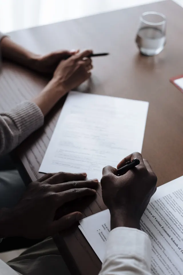 Hands signing a document next to a laptop